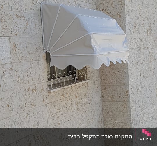 סוכך מרקיזה מתקפל מותקן מעל חלון בקיר אבן
